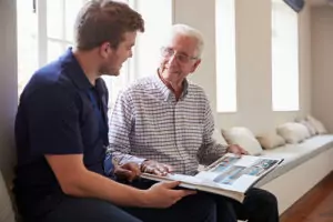 the adult male holds a photo album with a senior male providing the senior male with senior memory support